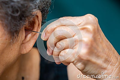 Senior woman putting earpick into her left ear, Grey curly hairs, Swimming pool background, Healthcare, Symptom of hearing loss Stock Photo