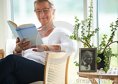 Senior, woman and relaxing with book in home for reading, wellness or self care. Elderly person, glasses and smile with Stock Photo