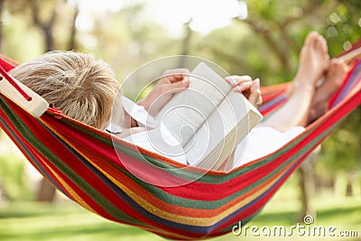 Senior Woman Relaxing In Hammock With Book Stock Photo