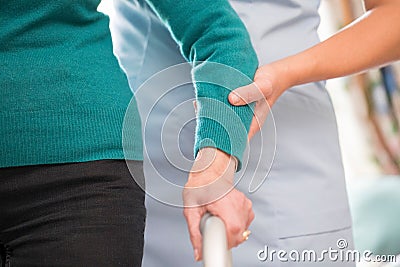 Senior Woman`s Hands On Walking Frame With Care Worker In Backgr Stock Photo