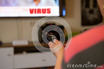 A senior woman sits in front of the television watching television. She holds a remote control in her hand that she points at the Stock Photo