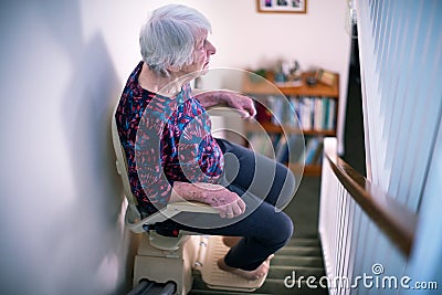 Senior Woman Sitting On Stair Lift At Home To Help Mobility Stock Photo