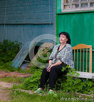 A senior woman sitting tired near her house in the village Stock Photo