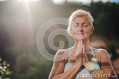 A senior woman standing outdoors on a terrace in summer, doing yoga. Stock Photo