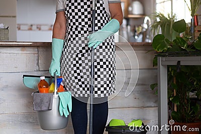 Senior woman standing and ready to start with the housework. Close to she a plastic bucket with items for cleaning. One alone Stock Photo