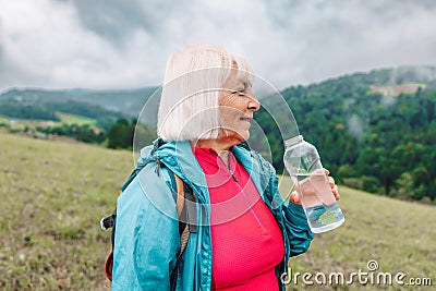 caucasian 50s blonde girl drinking water from plastic bottle. Mountain background Stock Photo