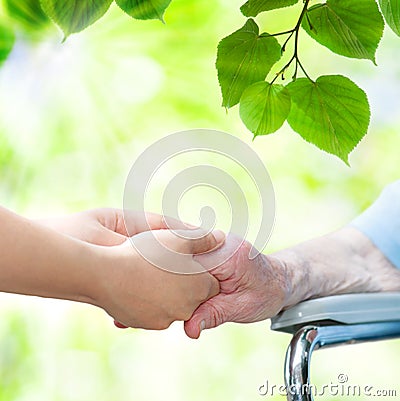 Senior woman in wheel chair holding hands with young caretaker Stock Photo