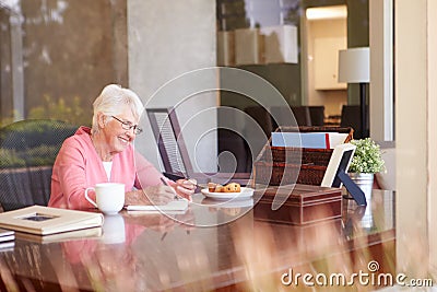 Senior Woman Writing Memoirs In Book At Desk Stock Photo