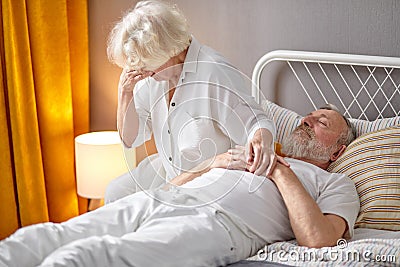 Senior woman sitting next to dying husband lying on bed and crying Stock Photo