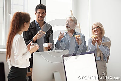 Senior and young colleagues talking while eating pizza in office Stock Photo