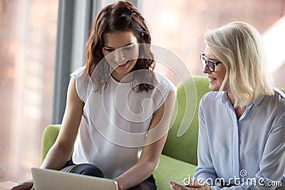 Senior and young colleagues women sitting looking at laptop scre Stock Photo