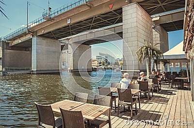 Seniors, young people refreshing and drinking at river restaurant near concrete bridge Editorial Stock Photo