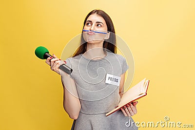 Half-length portrait of young girl, correspondent holding reporter microphone isolated on yellow studio background Stock Photo
