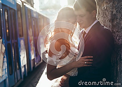 Sensitive portrait of the happy newlywed couple hugging and leaning on the wall at the background of the driving tram Stock Photo
