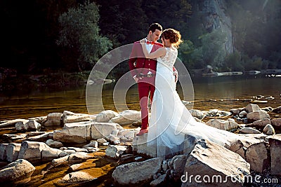 Sensitive portrait of the wedding couple hugging on the riverstones during the sunset. Horizontal shot. Stock Photo