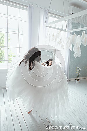 Sensual and beautiful young girl in bridal lingerie and angel wings looking in the mirror Stock Photo