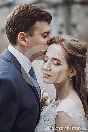 Sensual groom kissing beautiful bride on the forehead, newlywed couple portrait, beautiful married couple posing outdoors Stock Photo