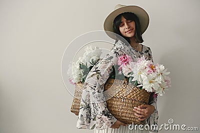 Sensual portrait of boho girl holding pink and white peonies in rustic basket. Stylish hipster woman in hat and bohemian floral Stock Photo