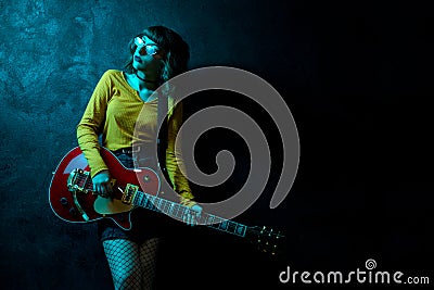 Sensual young hipster woman with curly hair with red guitar in neon lights. Rock musician is playing electrical guitar Stock Photo