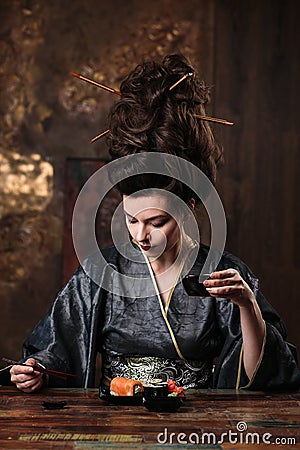 Sensual young woman in a geisha asian costume with fashion makeup and hair style drinks tea and eats sushi Stock Photo