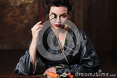 Sensual young woman in a geisha asian costume with fashion makeup and hair style eats sushi Stock Photo