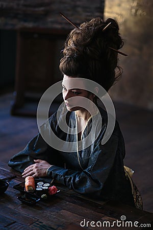 Sensual young woman in a geisha asian costume with fashion makeup and hair style eats sushi Stock Photo