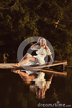 Sensual young woman sitting by the lake at sunset or sunrise posing Stock Photo