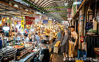 View of an alley of the Kwangjang market at night with people eating street food at stalls Editorial Stock Photo