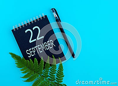 September 22th. Day 22 of month, Calendar date. Black notepad sheet, pen, fern twig, on a blue background Stock Photo