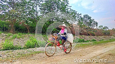 Serang, Indonesia, Friday, October 20 2023 a woman rides a bicycle while carrying a sack on the back and wearing a hat Editorial Stock Photo