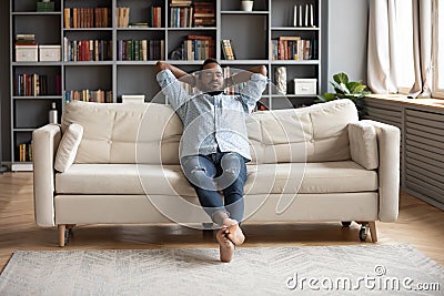 Serene barefoot african man resting on sofa hands behind head Stock Photo