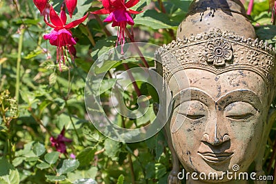 Serene Buddha face. Garden statue with fuschia flowers. Nature Buddhism Stock Photo