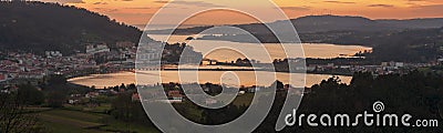 Serene dusk panorama of the medieval fishing town of Pontedeume with its iron and stone bridge orange sky La CoruÃ±a Galicia Stock Photo