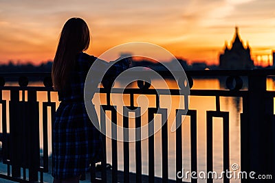 Serene girl standing alone on waterfront in front of fence of embankment. Stock Photo