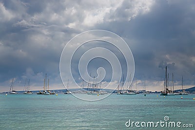 A serene seascape in Mallorca with multiple sailboats, peacefully anchored on calm turquoise waters Stock Photo