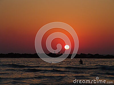 Serene summer sunset over Tel Aviv sea beach, in vivid orange colors with silhouettes of people swimming, fishing and walking on Stock Photo