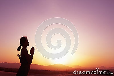 Serene young woman with hands together in prayer pose in the desert in China, silhouette, profile, sun setting Stock Photo