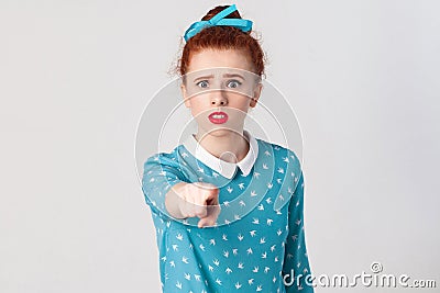 The seriosly redhead girl, wearing blue dress, opening mouths widely, having surprised shocked looks, pointing finger at camera. Stock Photo