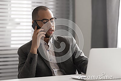 Serious African American businessman talking on phone, using laptop Stock Photo