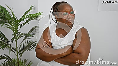 Serious african american woman, a successful manager with braids and glasses, sits relaxed yet concentrated in the waiting room, Stock Photo