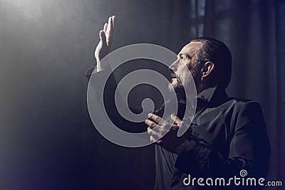 A serious bearded man on dark background indoor, black and white effect. Hansome middle-aged man profile looking to light Stock Photo