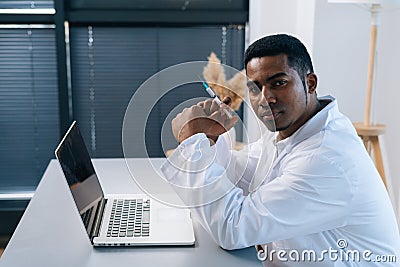 Serious black male doctor in white uniform thoughtful looking at camera holding in hand syringe with vaccine in hand Stock Photo