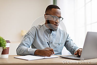 Serious Black Man Writing Business Report At Laptop In Office Stock Photo