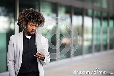 Serious black middle aged boss standing outside office building, holding cellphone and reading message outdoors Stock Photo