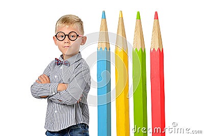 Serious boy in glasses and bowtie posing near huge colorful pencils. Educational concept. Isolated over white. Stock Photo