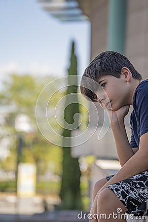 Serious boy thinking over a problem and contemplating sitting on a fence. Real people concept Stock Photo