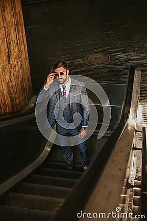 Serious businessman going up on the escalator while holding sung Stock Photo