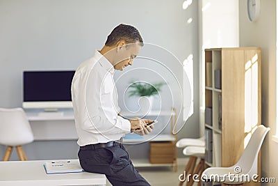 Serious businessman standing in the office and using finance app on his mobile phone Stock Photo