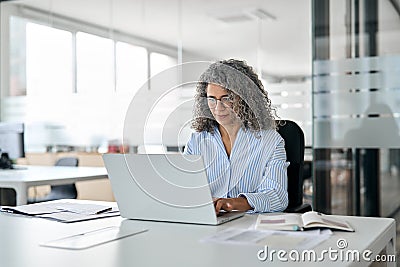 Busy mature professional business woman looking at laptop working in office. Stock Photo