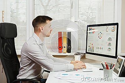 Serious and engrossed business man in shirt sitting at the desk, working at computer with modern monitor. Manager or worker. Stock Photo